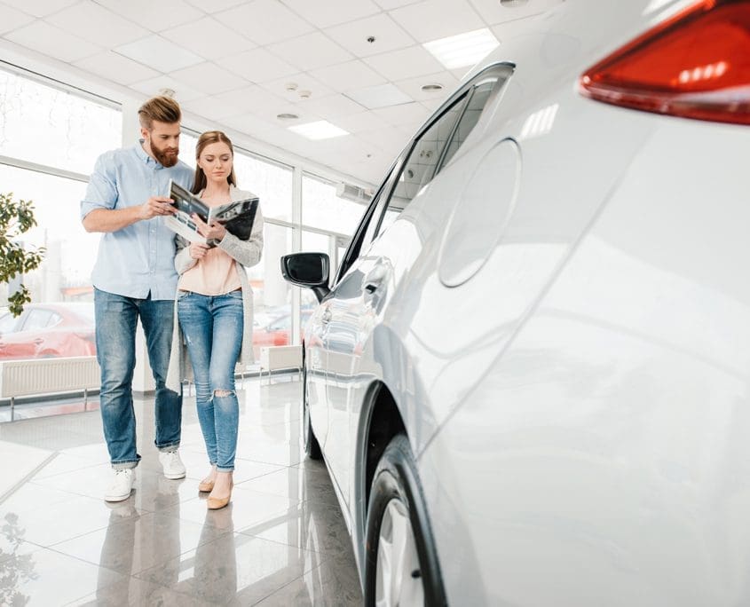 Car Valuations Melbourne - Happy couple holding catalog and choosing car in dealership