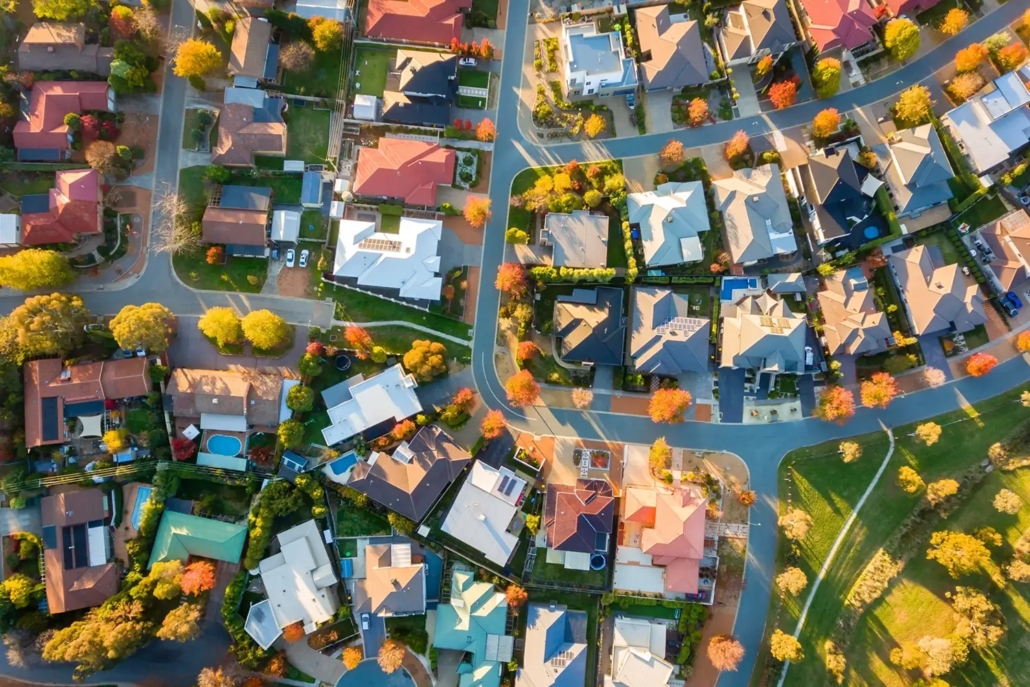 Property Valuations by Asset Valuations Group - Aerial view of a suburban neighbourhood with houses, curved streets, green lawns, and vibrant autumn trees. Sunlit backyards—some with pools—highlight why you might wonder: Why Do I Need a Property Valuation in such a picturesque setting?.