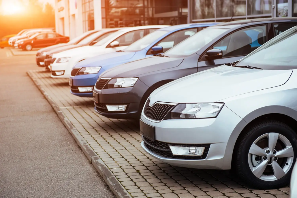 A row of parked cars in various colors lined up outside a dealership building at sunset, with the sun casting a warm glow—perfect for accurate vehicle valuations Brisbane buyers can trust.