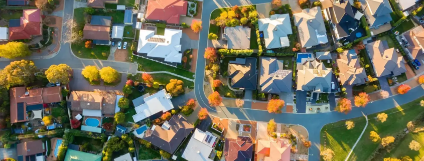 Aerial view of a suburban neighborhood with winding streets, houses of various colored roofs, scattered trees, and small yards—an organized autumn residential area ideal for Property Valuations Rockhampton.