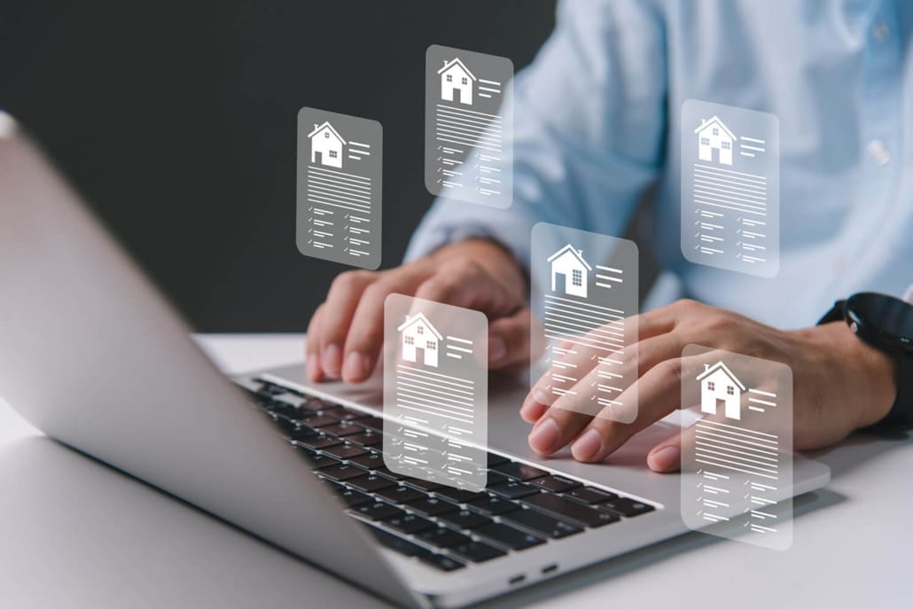 A person types on a laptop keyboard with digital icons of house documents floating above, representing online real estate, property management, or Property Valuations Rockhampton.