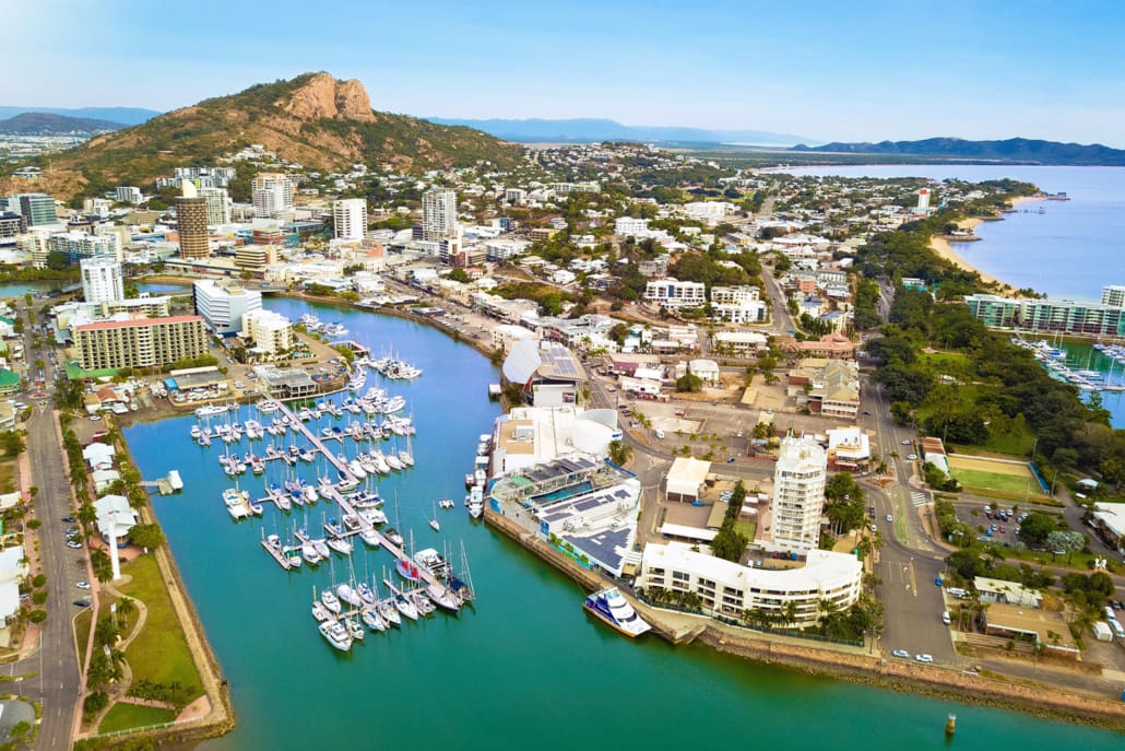 Aerial view of coastal Townsville with a marina full of boats, high-rise buildings, and green hills in the background—perfect for Valuations Townsville, set by the ocean and iconic rocky mountain landmark.