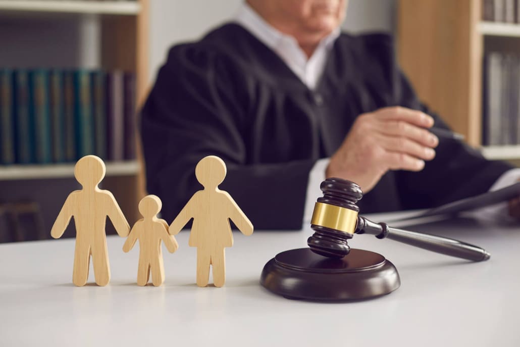 Compliant With Family Court Requirements Compliant With Family Court Requirements - A judge sits at a desk with a gavel, holding documents. In the foreground are wooden cutouts of two adults and a child, symbolizing a family, suggesting a legal decision involving family law.