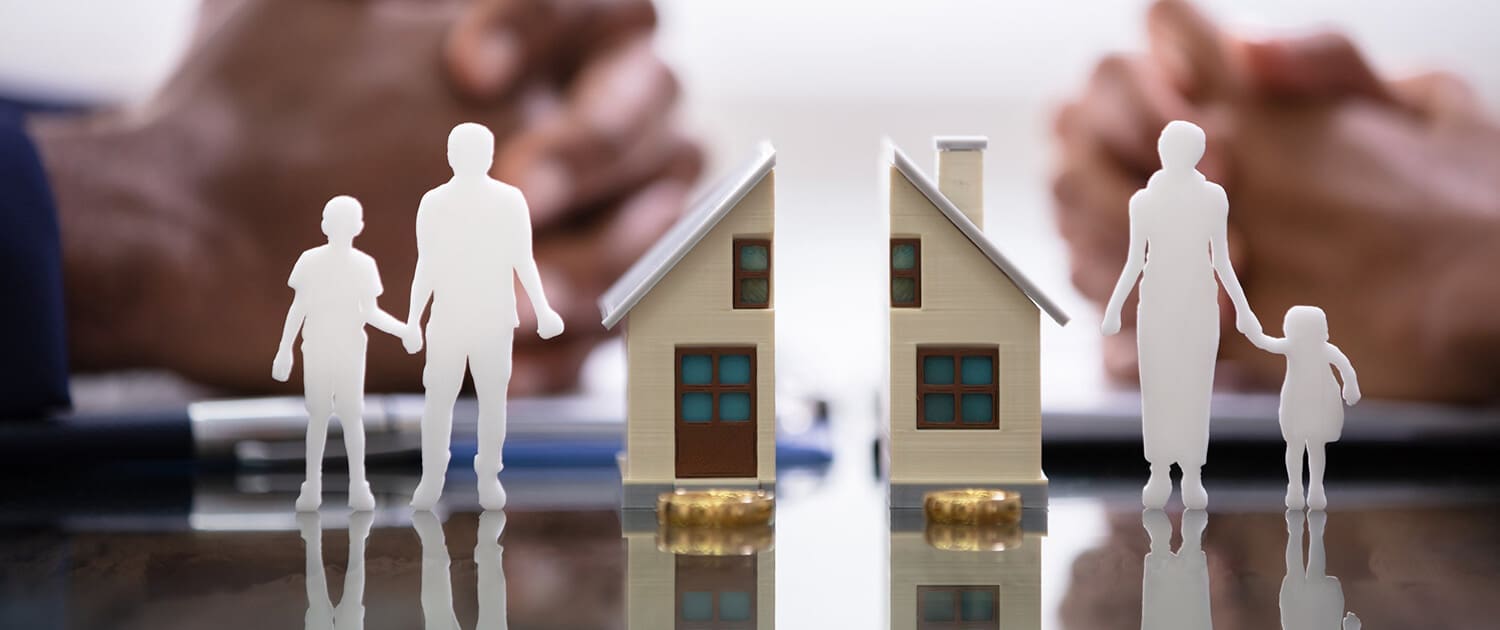 Family-Law-Valuations-AVG-Desktop Paper cutouts of a family and a house are separated by stacks of coins, symbolizing division of assets, with two people’s hands clasped in the background, suggesting a discussion or negotiation, possibly about divorce or separation.