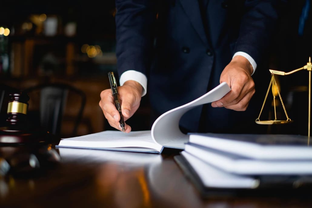 Valuations for Legal Representatives Individuals Valuations for Legal Representatives Individuals - A person in a suit signs a document on a desk with legal books, a gavel, and a scale of justice, suggesting a legal or law office setting.