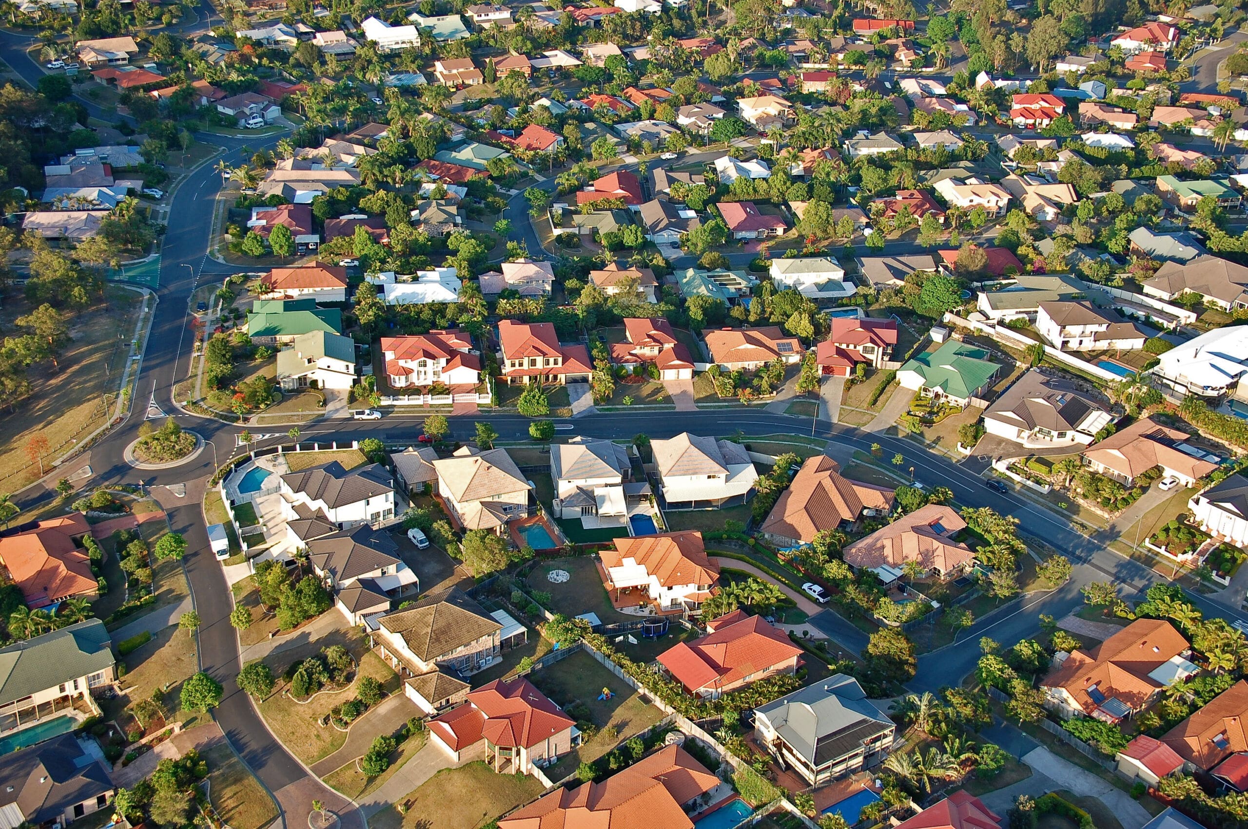 Property Valuations Brisbane Southside Property Valuations Brisbane Southside, Aerial view of a suburban neighborhood with neatly arranged houses, tree-lined streets, green lawns, and winding roads on a sunny day—ideal for anyone seeking Property Valuations Brisbane Southside amid vibrant greenery and varied roof colors.