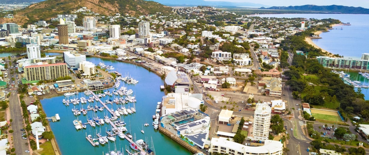 Valuations Townsville, Aerial view of Valuations Townsville, a coastal city with a marina full of boats, modern buildings, and a prominent rocky hill in the background under a clear blue sky.
