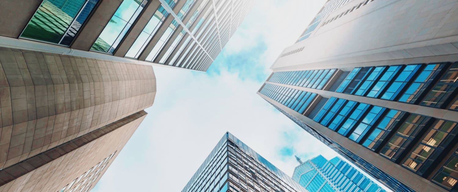 what factors affect a property valuation, A view looking up at several tall skyscrapers with glass and concrete facades, converging toward a bright, cloudy sky—an impressive cityscape that hints at what factors affect a property valuation.