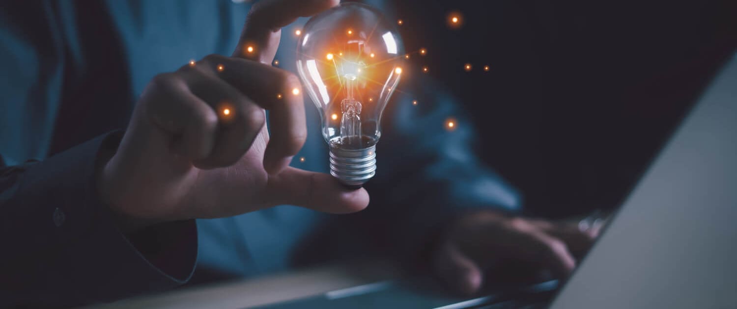 A person in a dark shirt holds a glowing light bulb with sparks near a laptop, symbolizing creativity and innovation in a technology or work setting—perfect imagery for Business Valuations Hervey Bay.