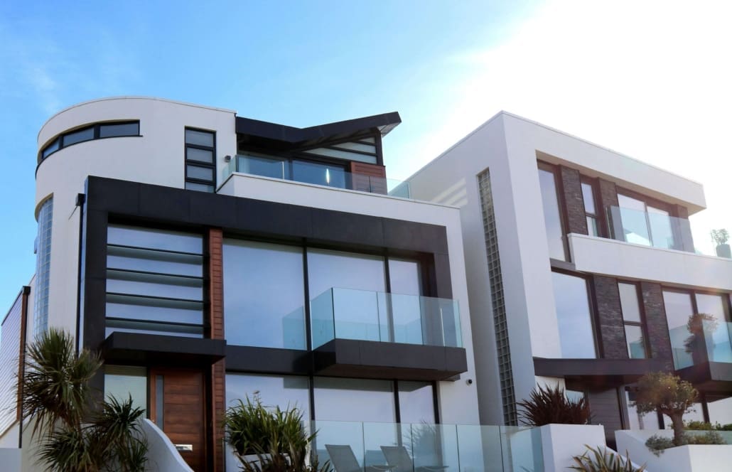 Modern white and black two-story house with large glass windows, glass balconies, and minimalist design features—ideal for Residential Investment Property CGT Valuations—set against a clear blue sky with palm plants in front.