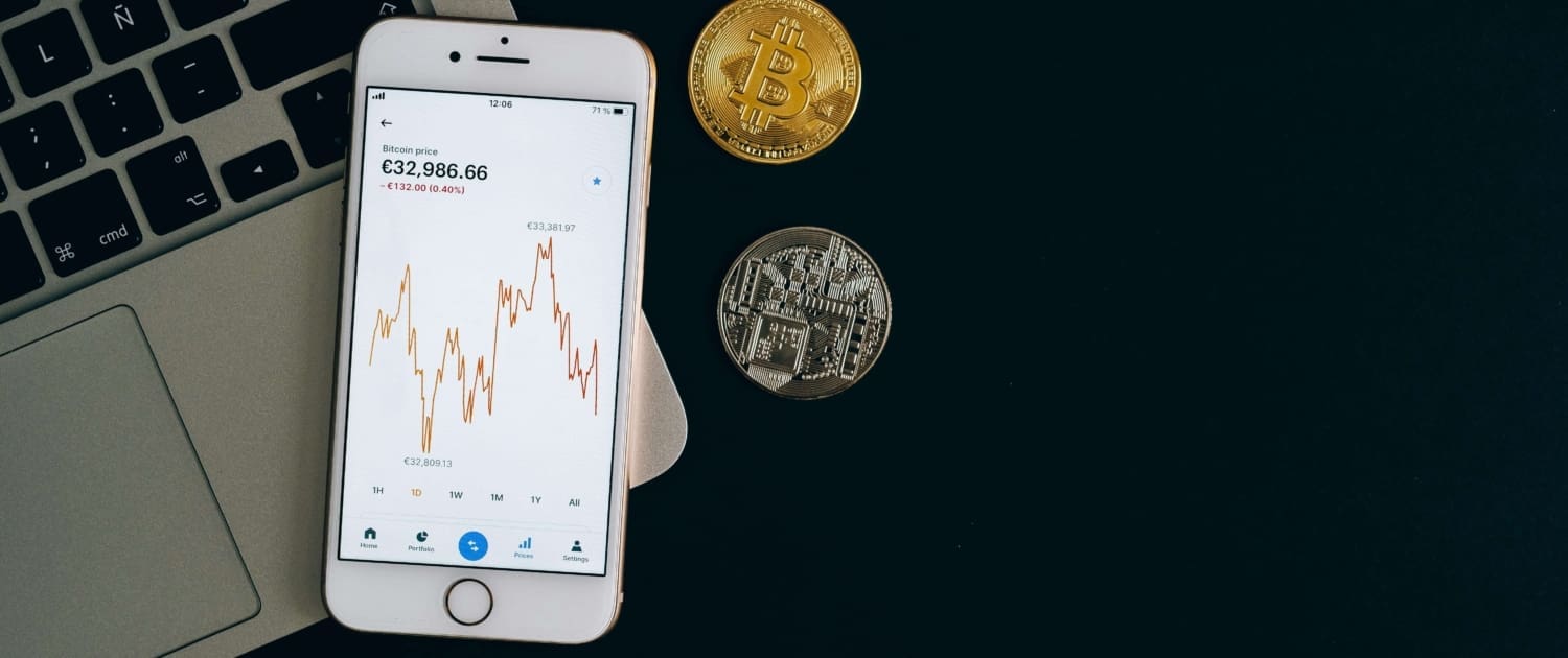 goodwill and Intangible Asset CGT valuations A smartphone displaying a fluctuating bitcoin price chart sits on a laptop keyboard, next to gold and silver coins, emphasizing the importance of accurate Goodwill & Intangible Asset CGT Valuations in today’s digital and crypto-driven economy.