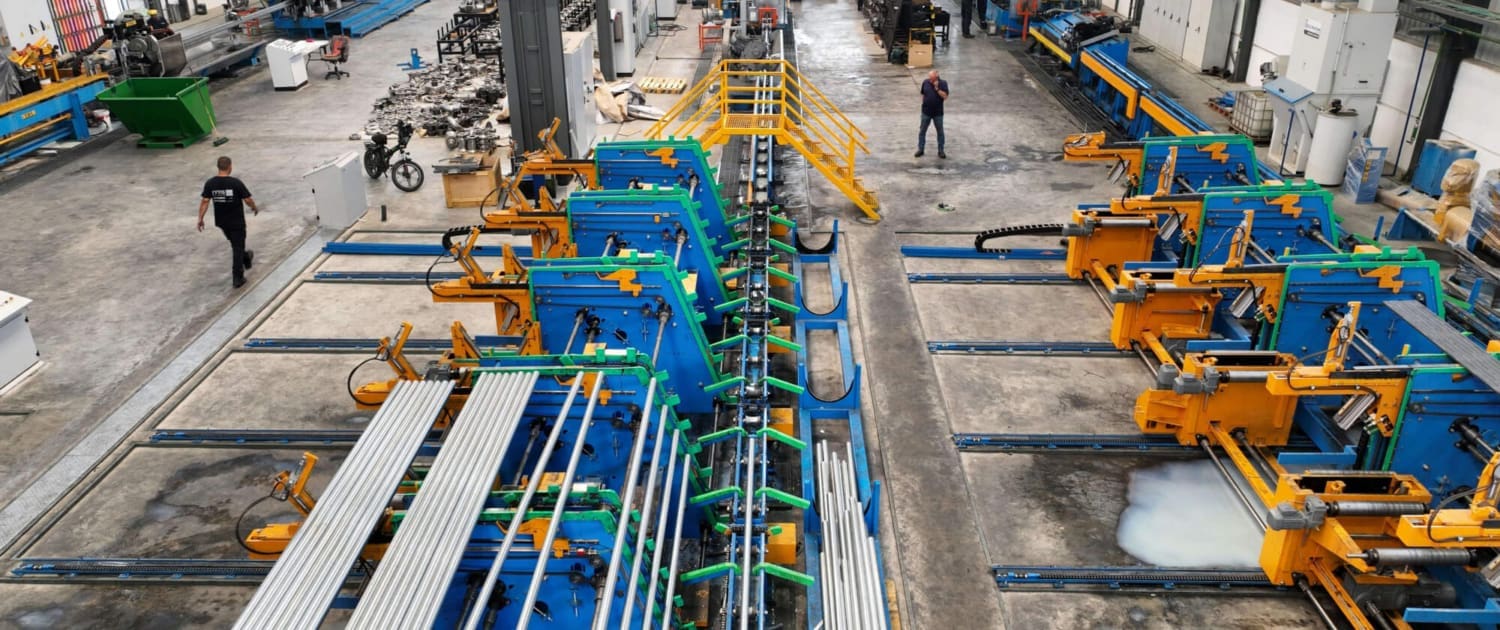 A large industrial factory floor with automated machinery, blue and yellow equipment, metal pipes, and a few workers in safety vests overseeing operations—ideal for Plant & Equipment CGT Valuations. The space is well-lit and meticulously organized.