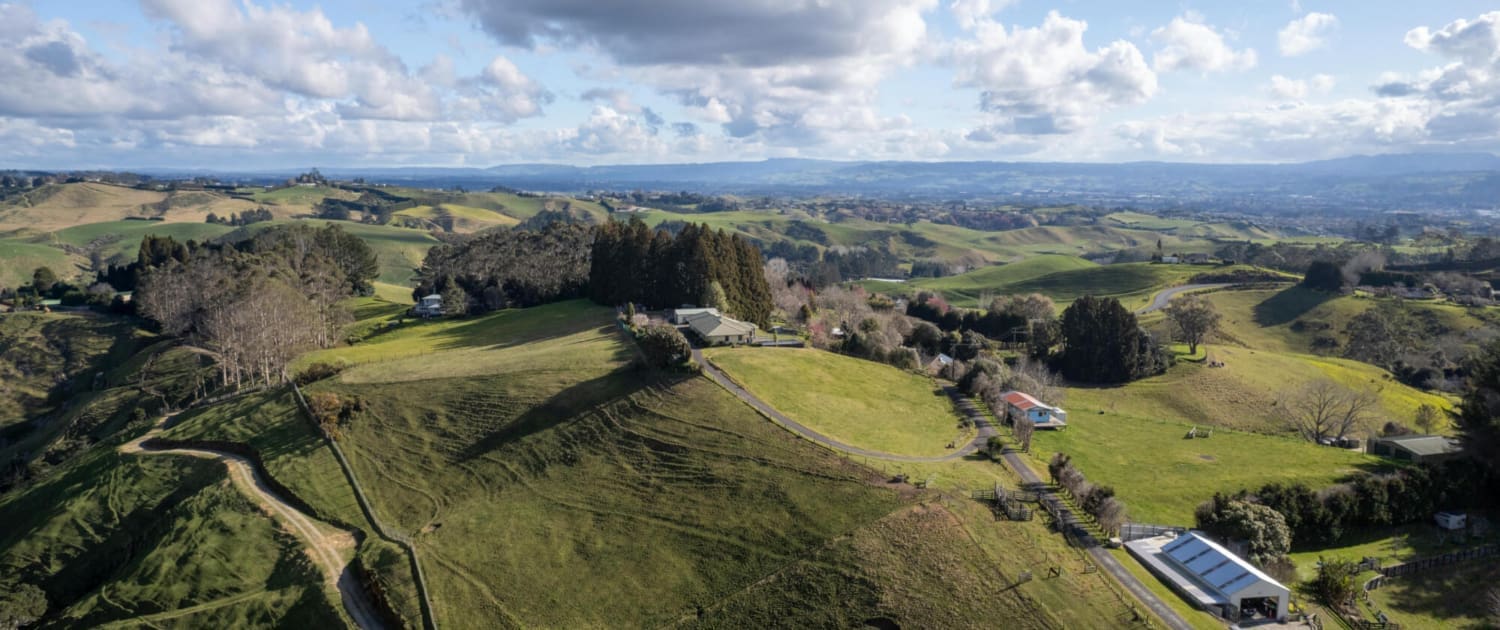 Aerial view of a green, rolling countryside with scattered houses, trees, winding roads, and fields—ideal for Rural Property CGT Valuations—under a partly cloudy blue sky.